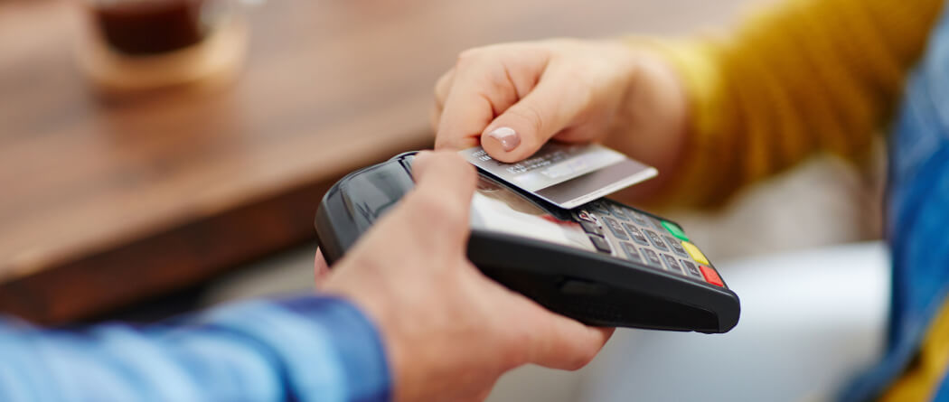 close-up of a person's hand holding a credit card up to a payment machine